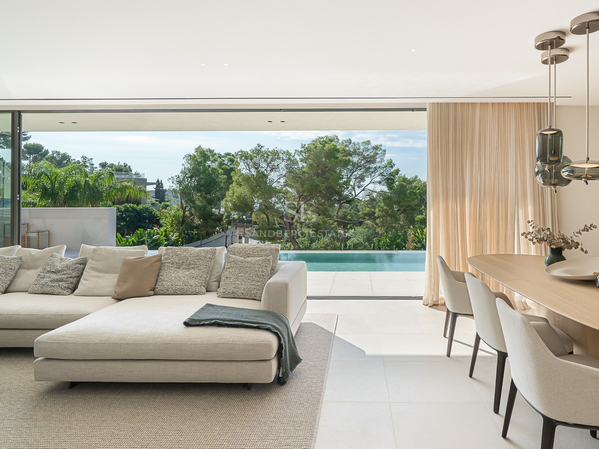 Salon moderne élégant avec canapé beige, coin repas et grandes baies vitrées ouvrant sur une terrasse avec piscine.