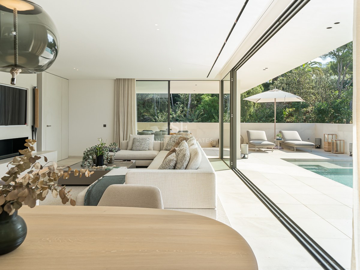 Salon moderne lumineux avec de grandes baies vitrées ouvrant sur une terrasse ensoleillée et une piscine privée.