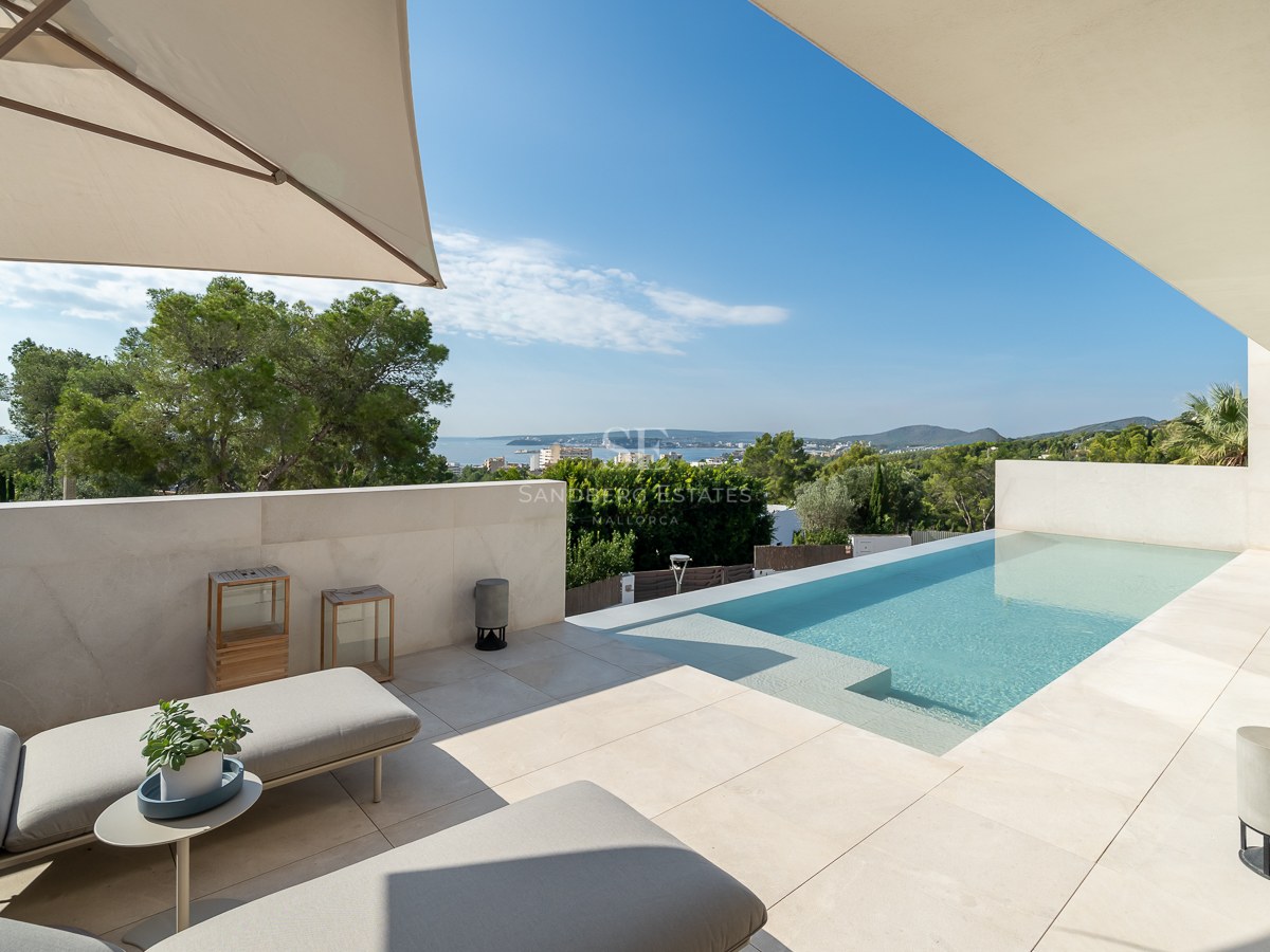 Chaises longues sur une terrasse moderne en pierre beige à côté d'une piscine offrant une vue sur la mer et la végétation.