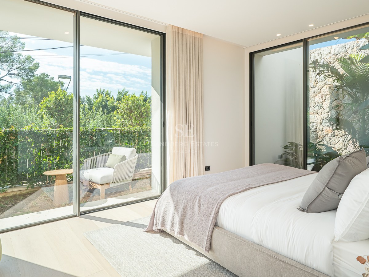 Chambre parentale lumineuse avec baies vitrées du sol au plafond donnant sur une terrasse privée verdoyante.