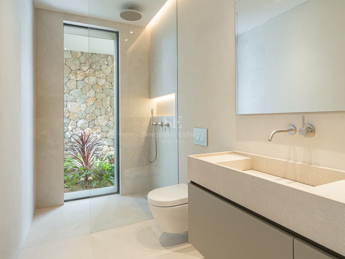 Salle de bain épurée avec double vasque en pierre, douche à l'italienne et fenêtre donnant sur un mur en pierre naturelle.