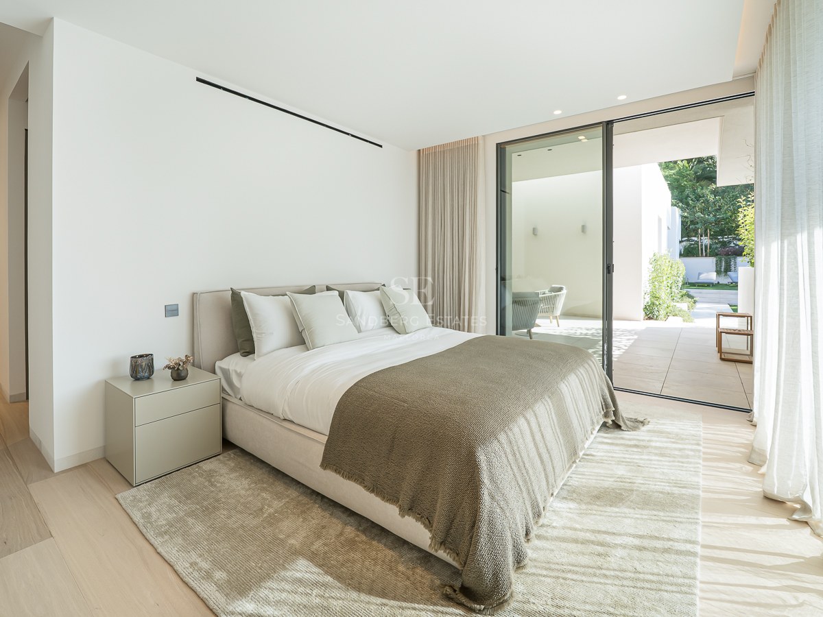 Chambre moderne avec grand lit, parquet clair et baies vitrées coulissantes ouvrant sur une terrasse privée.