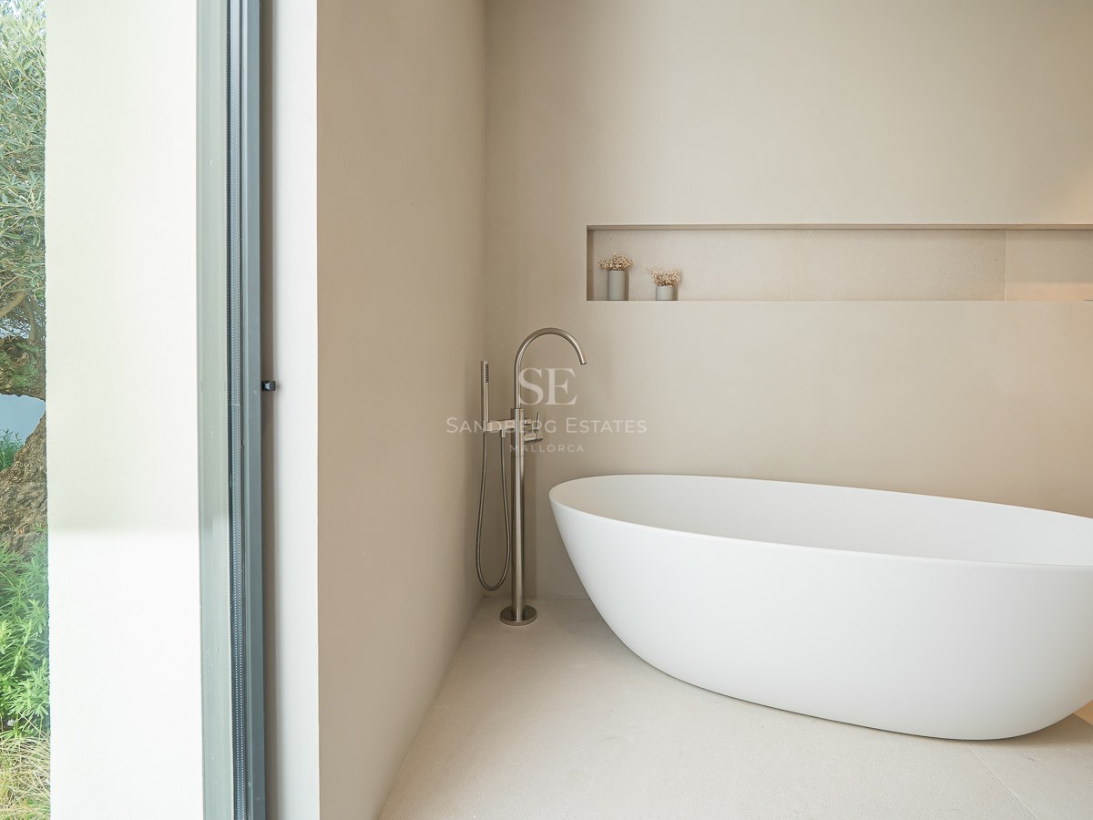 Salle de bain moderne avec baignoire îlot blanche et grande baie vitrée donnant sur un olivier.