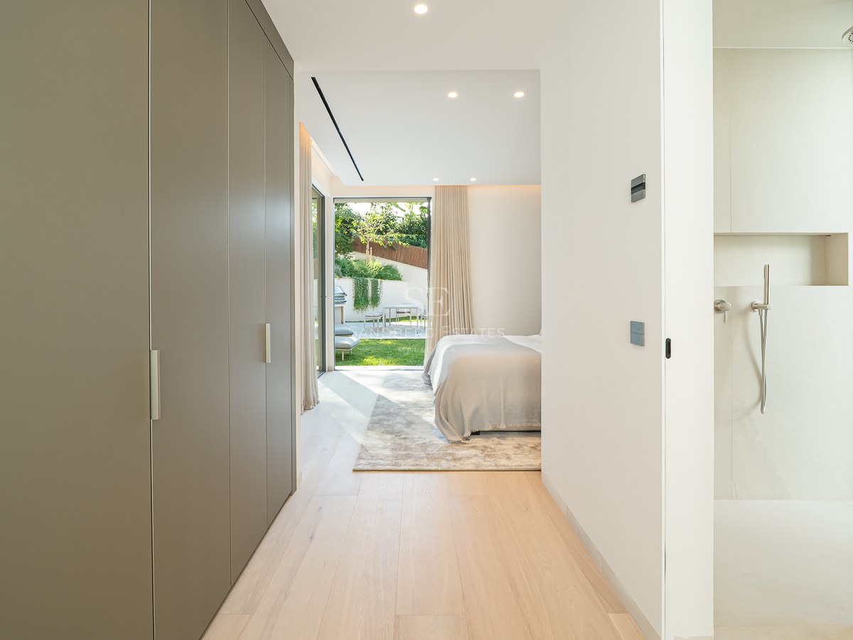 Couloir avec placards menant à une chambre moderne avec douche vitrée et accès direct à un jardin ensoleillé.