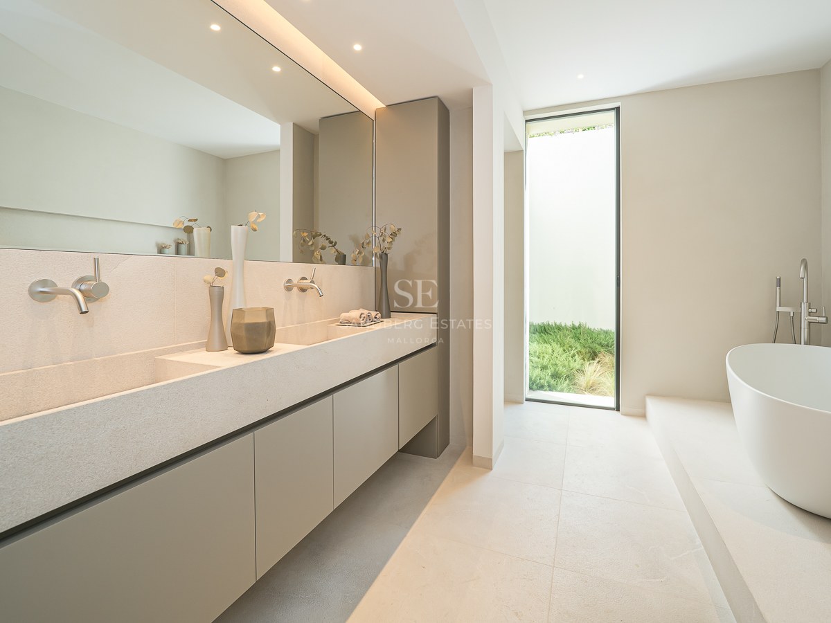 Salle de bain minimaliste avec double vasque en pierre, grand miroir, baignoire blanche et fenêtre sur le jardin.