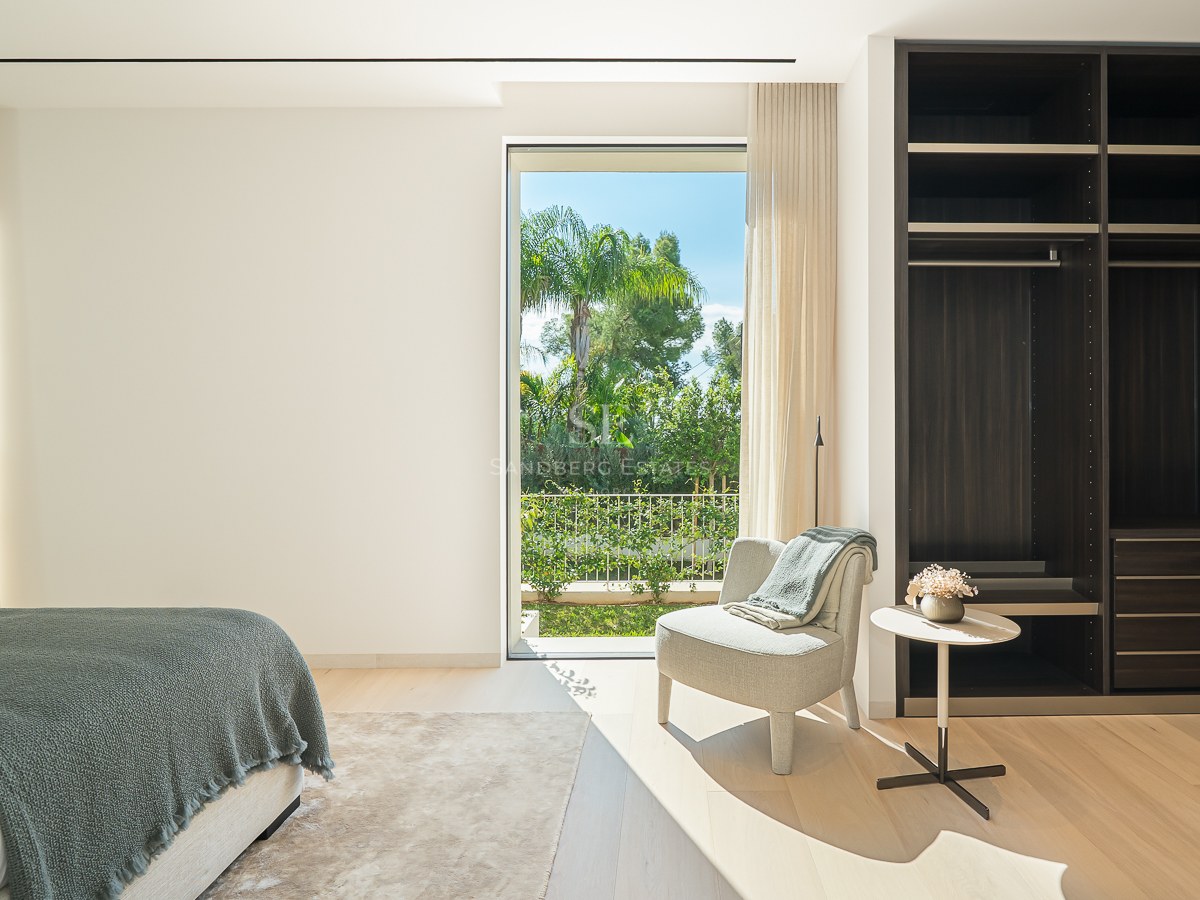 Chambre lumineuse avec un grand dressing en bois sombre, un fauteuil et une vue sur un jardin tropical.