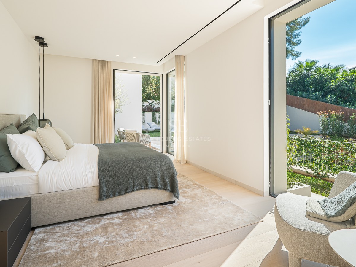 Chambre principale moderne avec grand lit, baies vitrées et vue sur un jardin luxuriant.