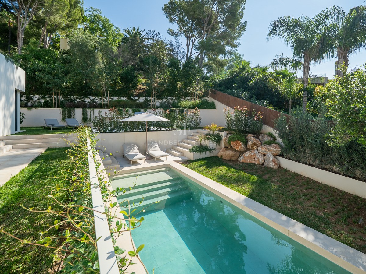 Piscine turquoise entourée d'une pelouse verdoyante, de murs blancs et d'une végétation luxuriante.