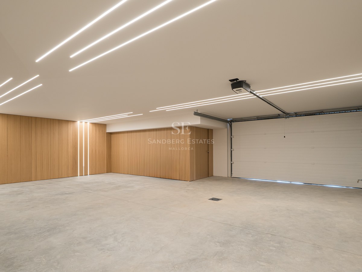 Vaste garage moderne avec sol en béton, panneaux muraux en bois et bandes lumineuses LED au plafond.