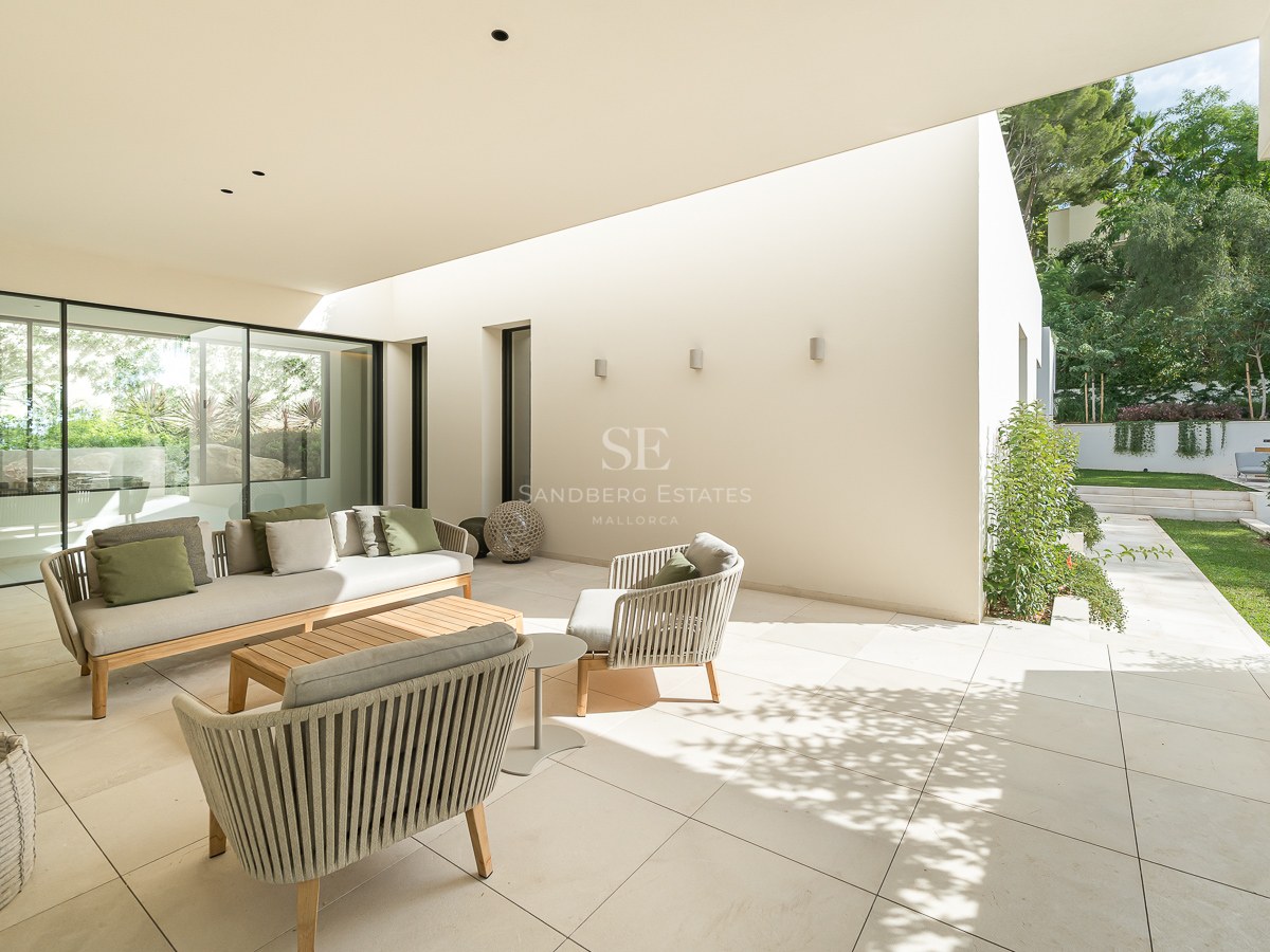 Terrasse de luxe avec canapé beige, coussins verts et chaises tressées sur un patio en pierre donnant sur le jardin.
