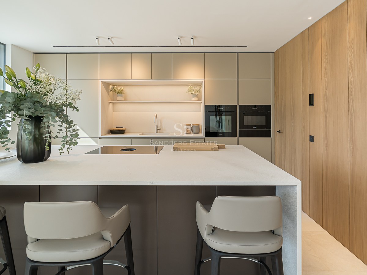 Îlot de cuisine moderne avec tabourets, appareils intégrés, mur en bois et fenêtre panoramique sur l'océan.