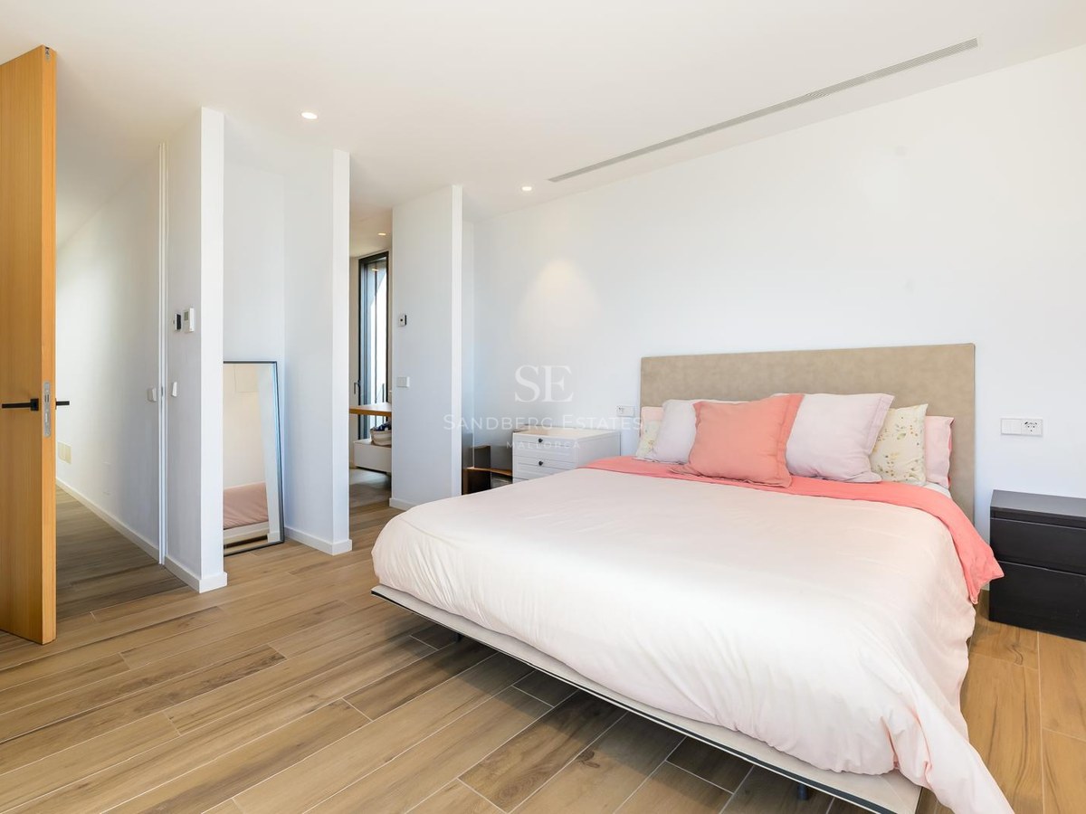 Dormitorio luminoso y moderno con una cama grande, cojines rosas, suelos de madera clara y paredes blancas.