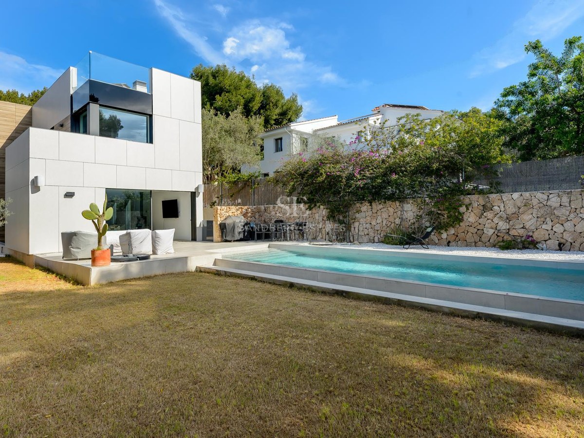 Villa blanca contemporánea con piscina rectangular, césped cuidado y muro perimetral de piedra natural bajo cielo despejado.