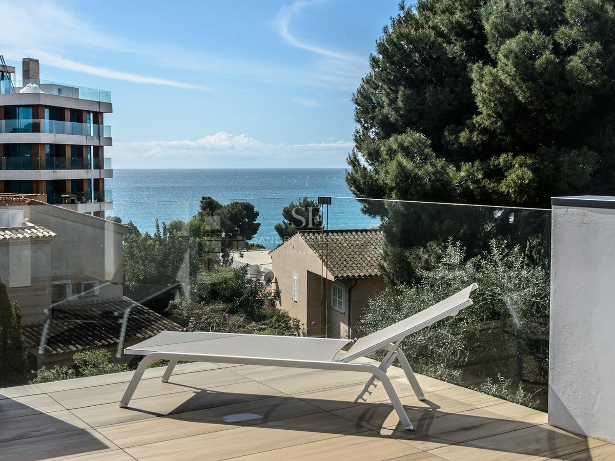 Tumbona blanca en terraza moderna con barandilla de cristal y vistas al mar Mediterráneo.