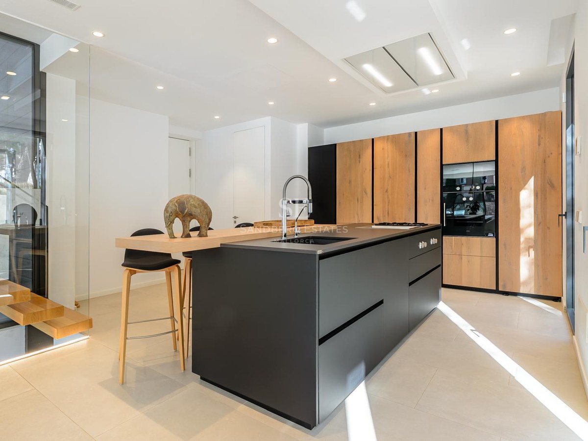 Cocina moderna con una gran isla negra, armarios de madera y electrodomésticos integrados bajo iluminación brillante.
