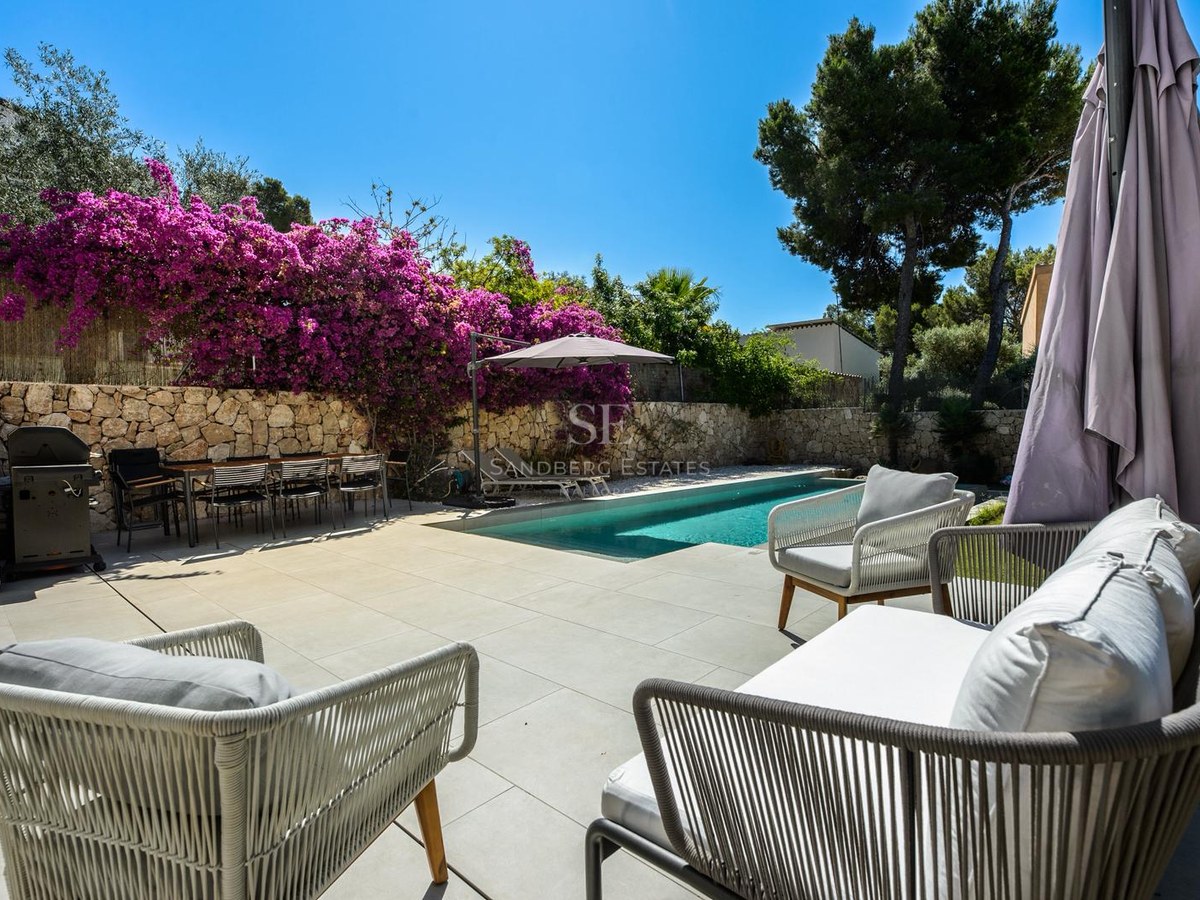 Zona de piscina privada con asientos de exterior, mesa de comedor, barbacoa y buganvillas púrpuras en muro de piedra.