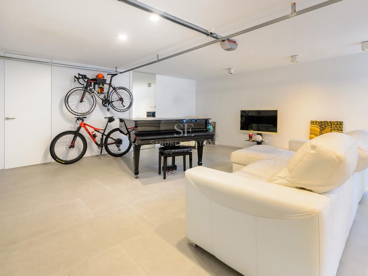 Sala moderna con un piano de cola negro, bicicletas montadas en la pared y un sofá de cuero blanco sobre suelo gris.