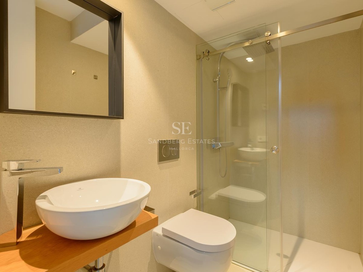 Baño contemporáneo con lavabo blanco sobre madera, inodoro suspendido y ducha de obra con mampara de cristal.
