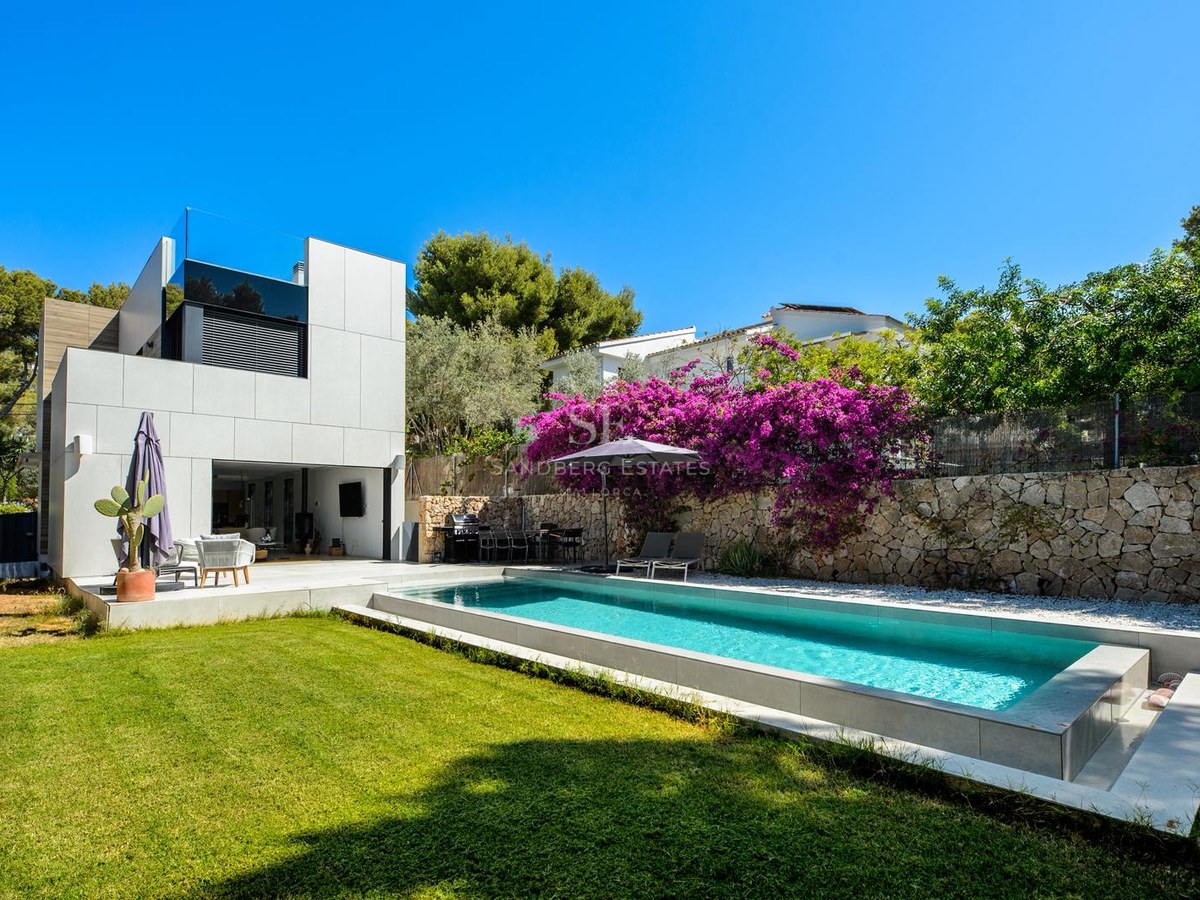 Piscina rectangular moderna junto a una villa blanca con buganvillas púrpuras y césped verde bajo un cielo azul.