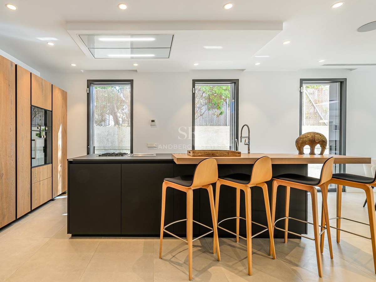 Cocina moderna con isla negra, barra de madera, cuatro taburetes y armarios de madera de suelo a techo.