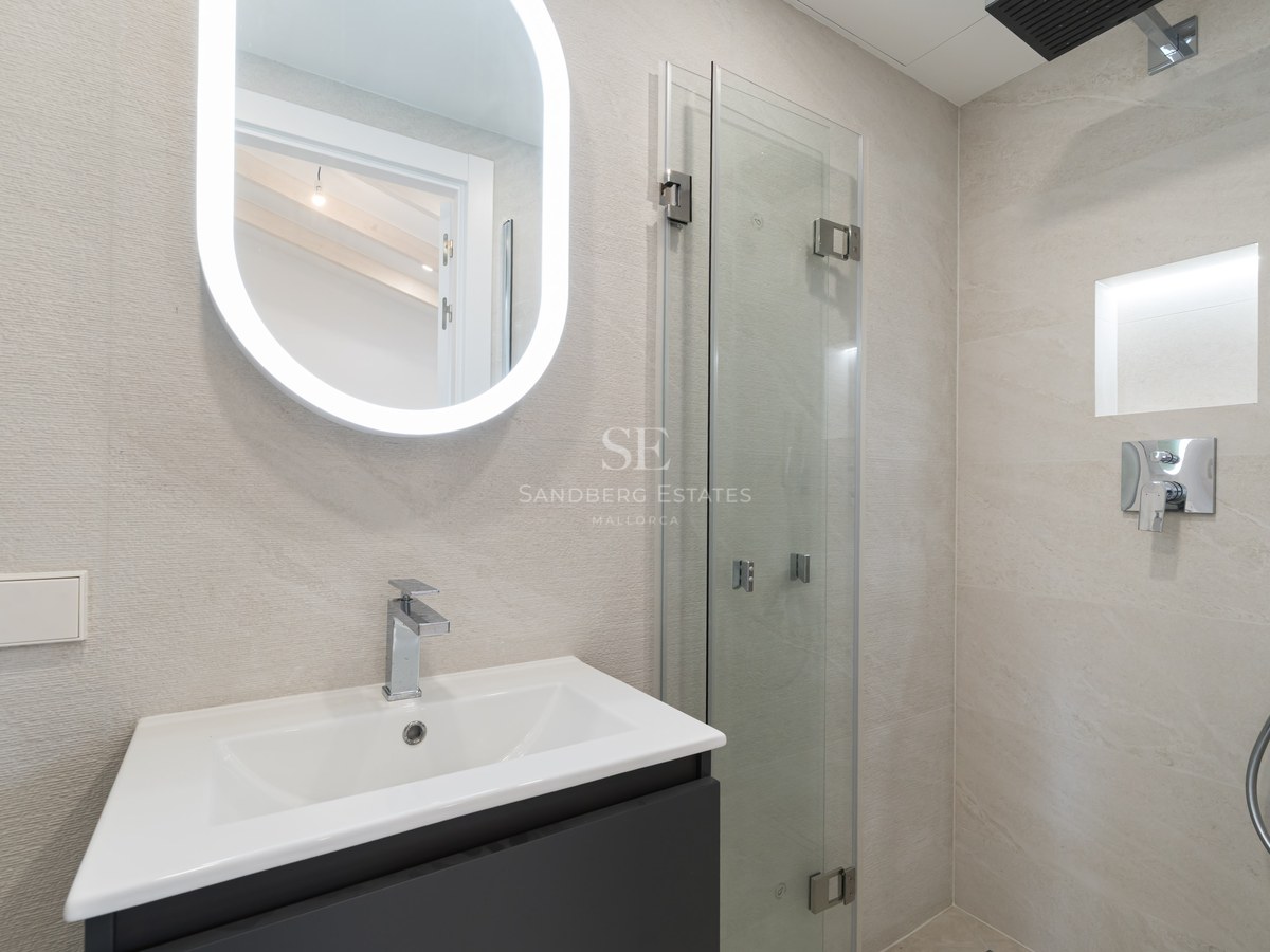 Modern bathroom vanity featuring a white sink, oval backlit LED mirror, and frameless glass shower enclosure.