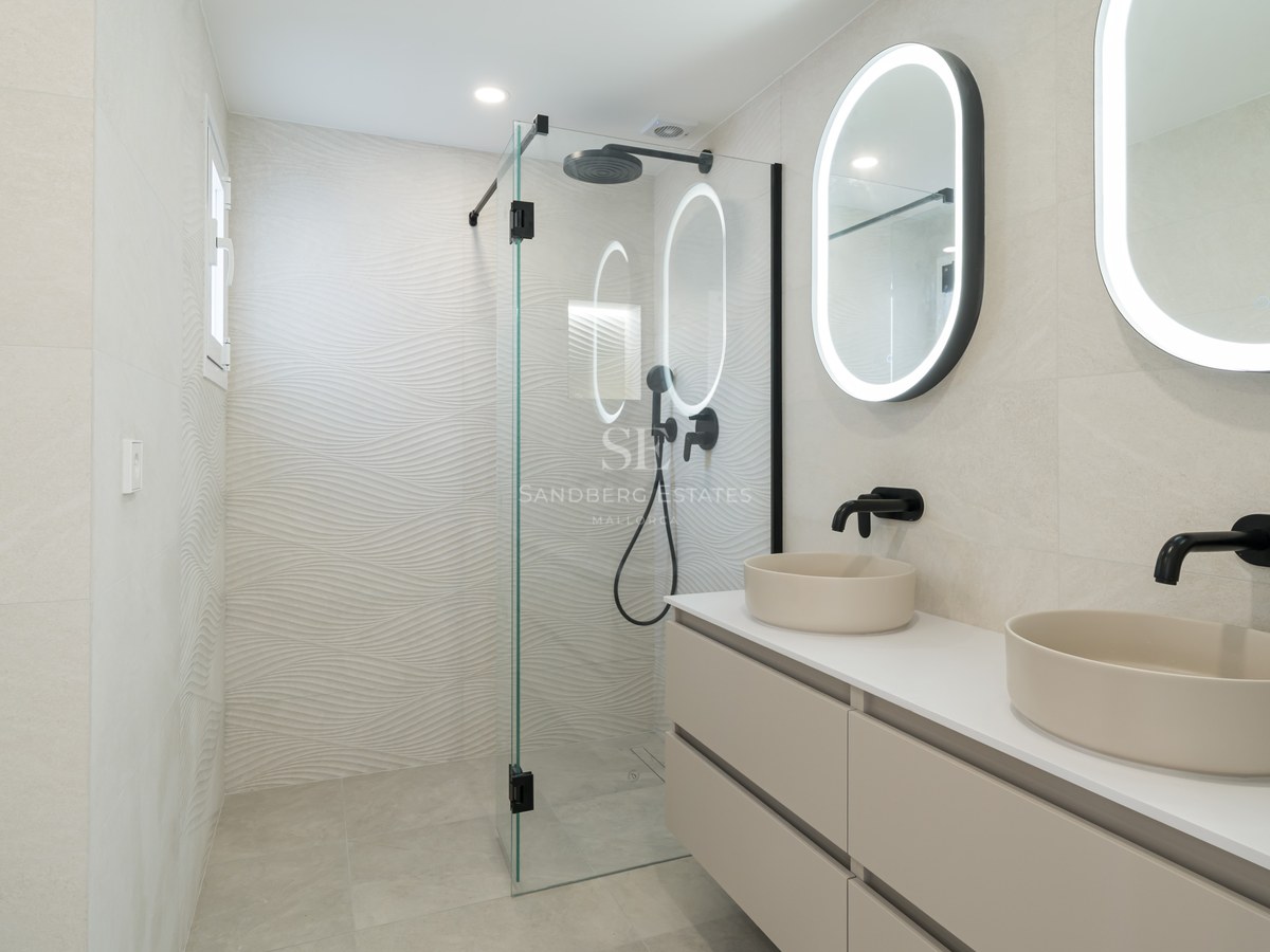 Minimalist bathroom featuring a walk-in glass shower, black faucets, and oval backlit mirrors over a floating vanity.