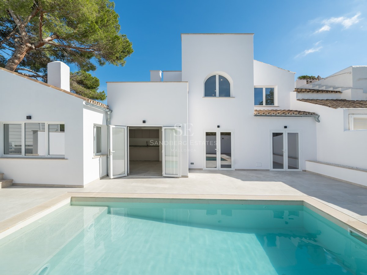Turquoise swimming pool in front of a clean white modern Mediterranean villa under a clear blue sky.