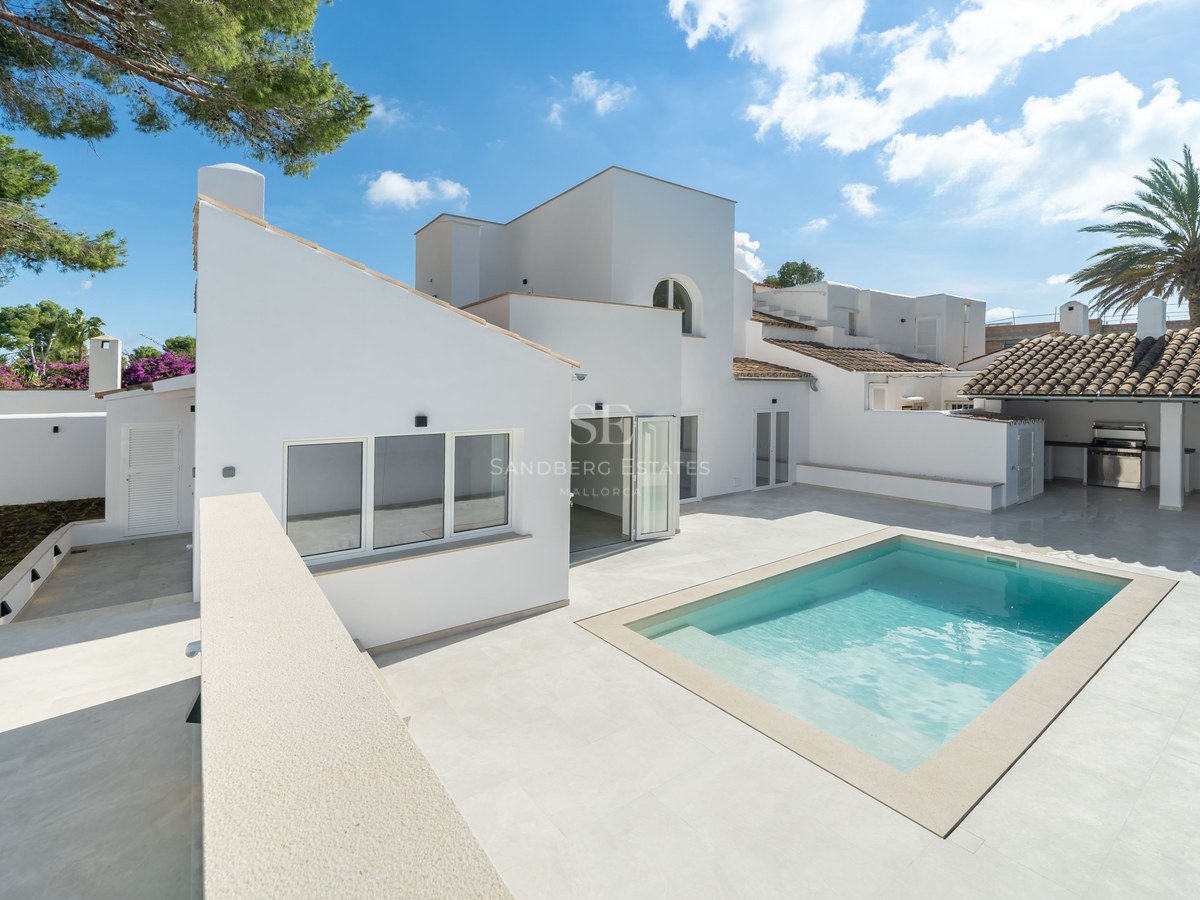 Modern white Mediterranean villa featuring a bright swimming pool, spacious stone patio, and outdoor kitchen area.
