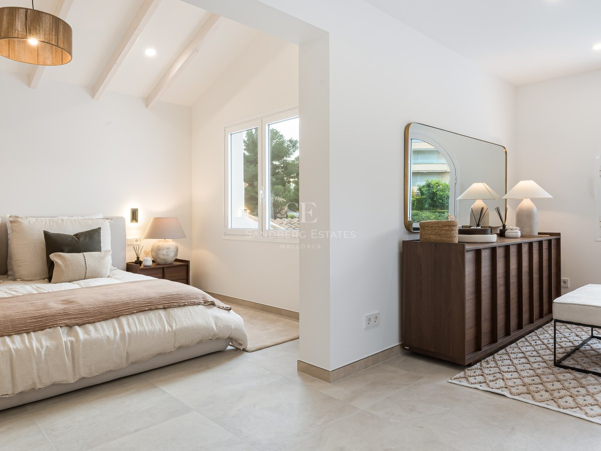 Modernt master bedroom med vita takbjälkar, stor säng, mörk träbyrå och naturligt ljus från fönster.