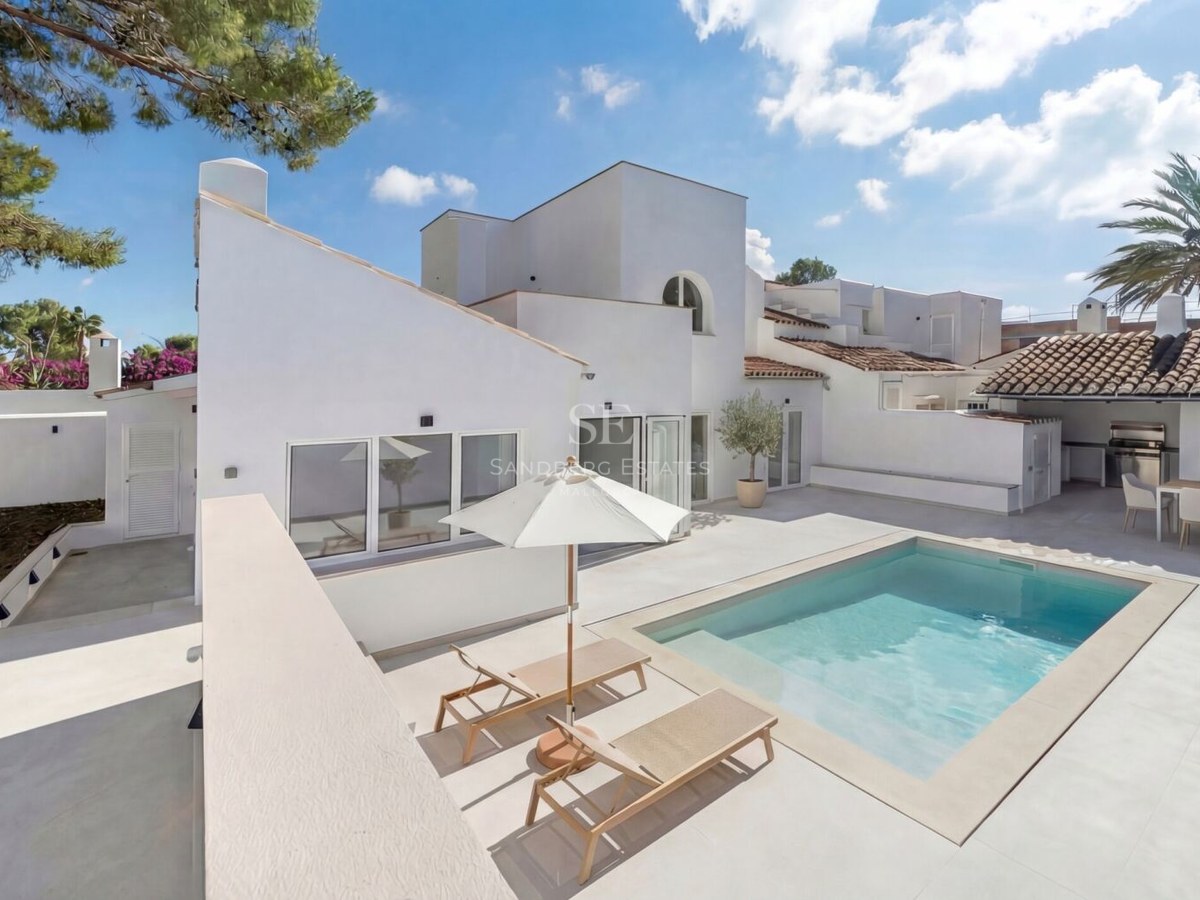 Modern vit villa med en rektangulär pool, solstolar och en utomhusmatplats under ett tegeltak.