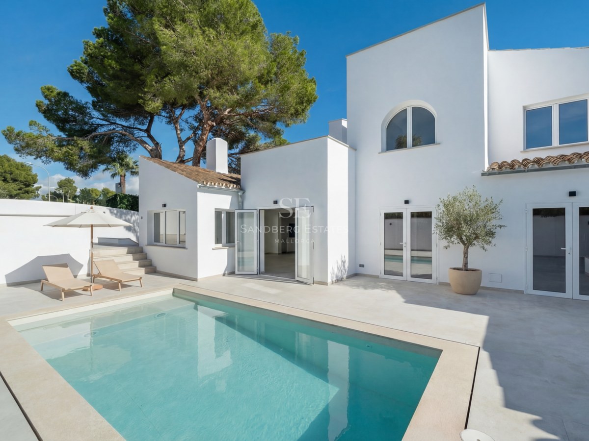 Modern vit villa med turkos pool, stenterrass och solsängar under en klarblå himmel.