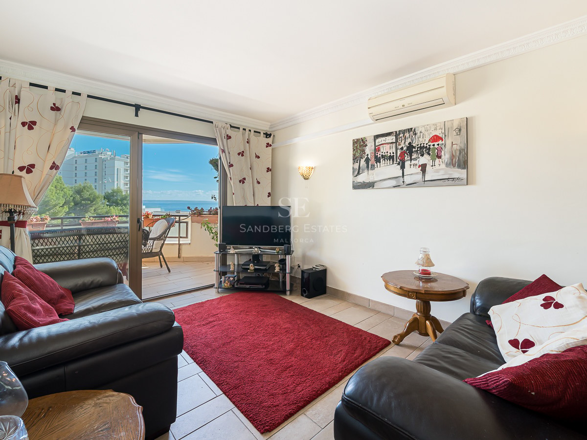 Living room with black leather sofas, a red rug, and a sliding door opening to a sea-view terrace.