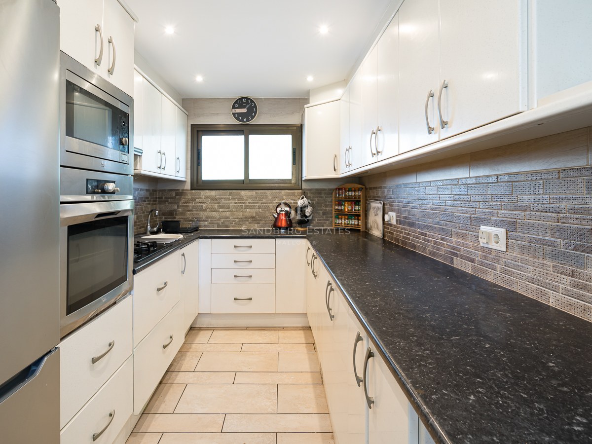 Galley kitchen featuring white cabinets, dark granite countertops, and built-in stainless steel appliances.