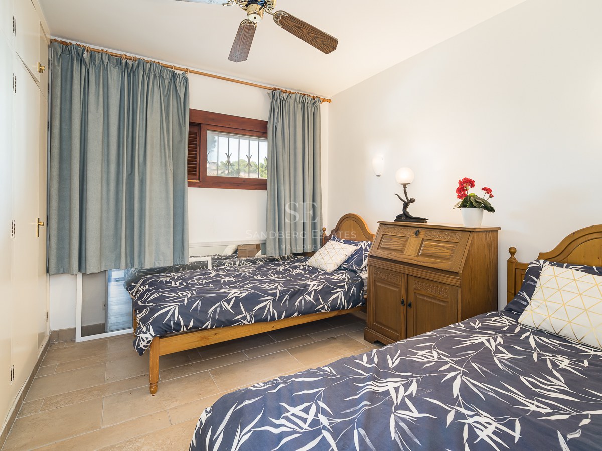 A bright bedroom featuring two wooden twin beds with blue patterned bedding, a ceiling fan, and large white wardrobes.