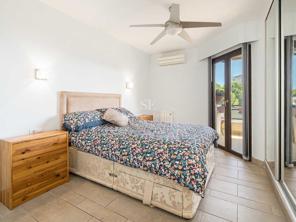 Bedroom featuring a double bed, wooden dresser, large mirrored closet, and a glass door leading to a sunlit balcony.