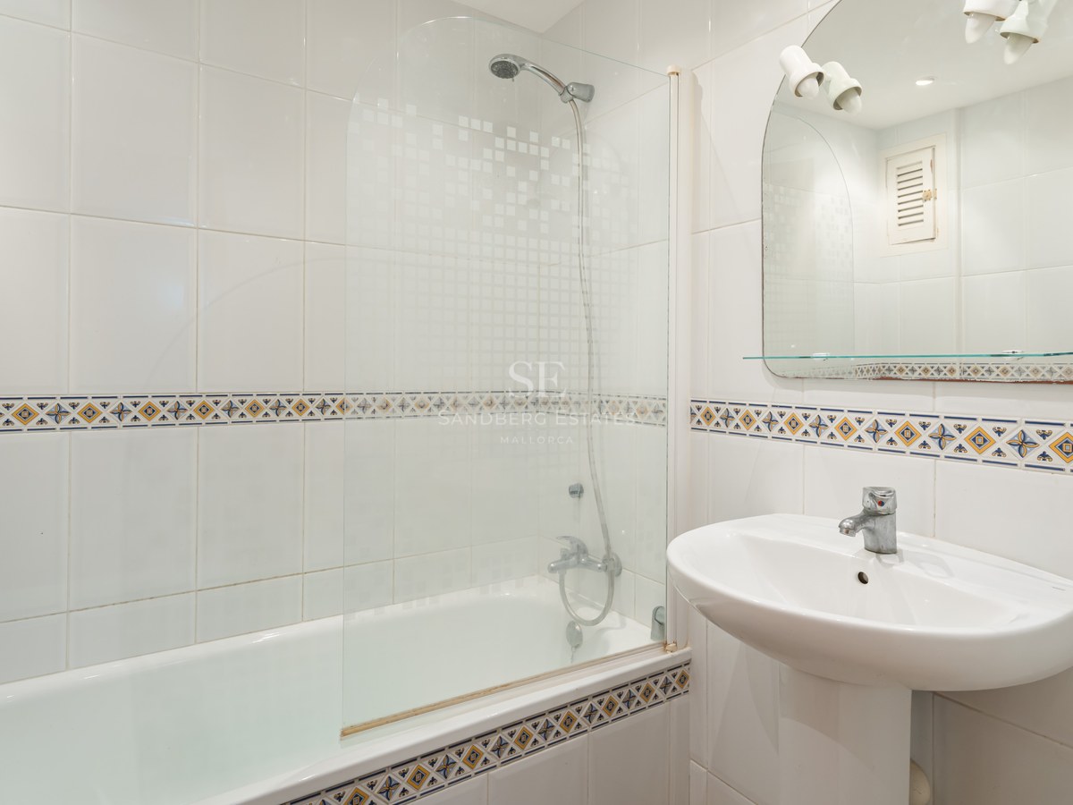 A white-tiled bathroom featuring a bathtub with a glass screen, a pedestal sink, and decorative border tiles.