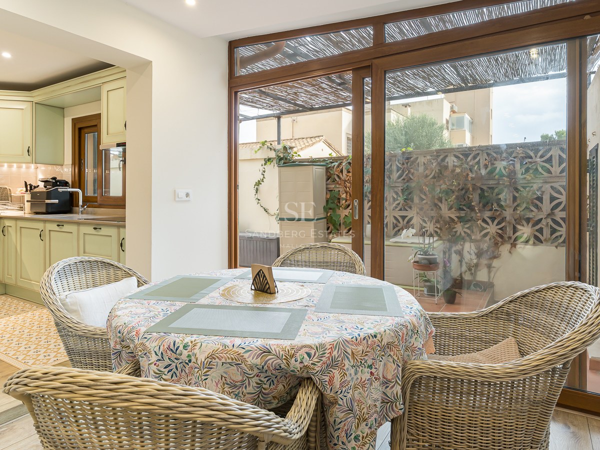 Dining table with wicker chairs next to a sage green kitchen and large sliding glass doors.