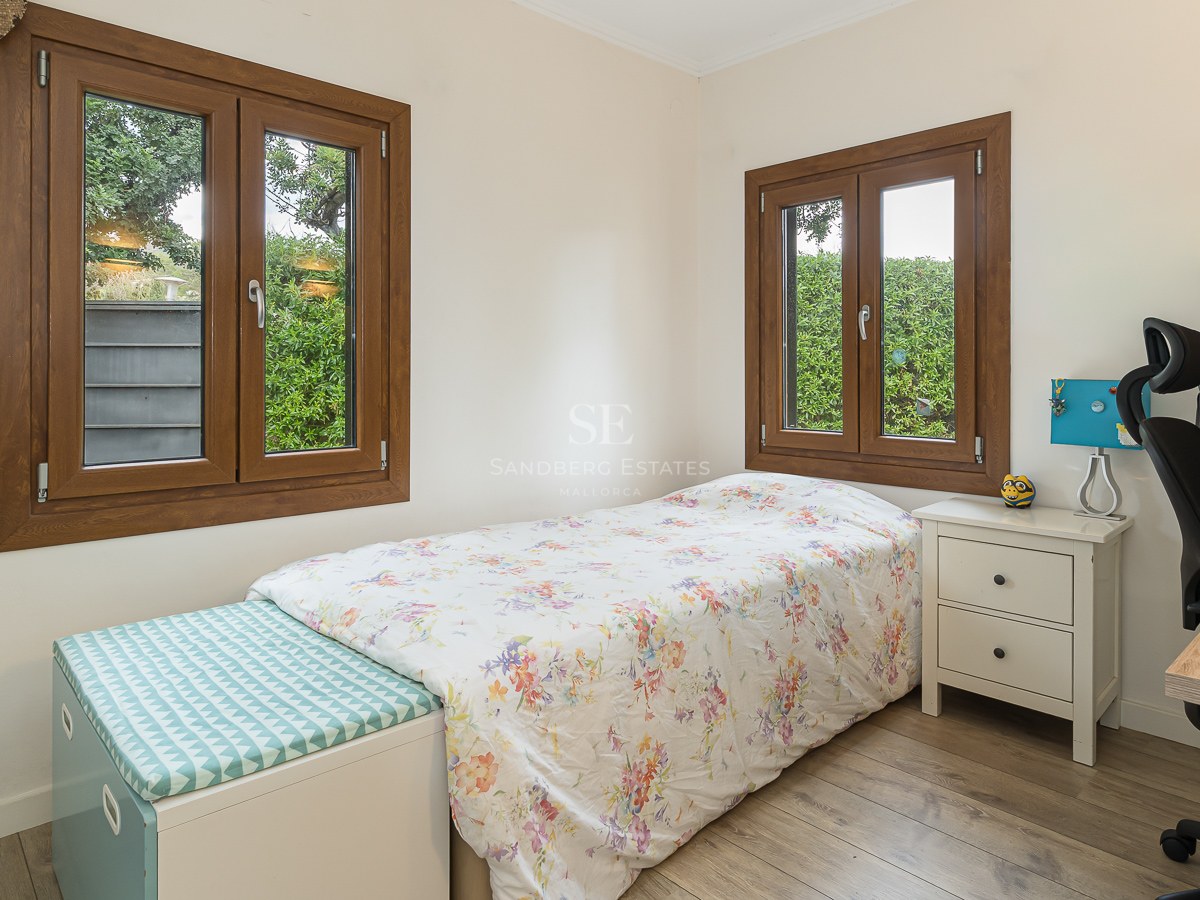 Bright bedroom with a single bed, desk, office chair, and wooden windows overlooking a green garden.