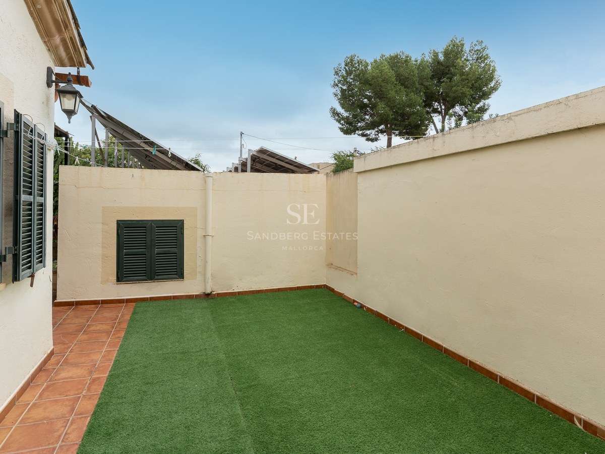 Small walled garden with artificial grass and terracotta tile border under a blue sky.
