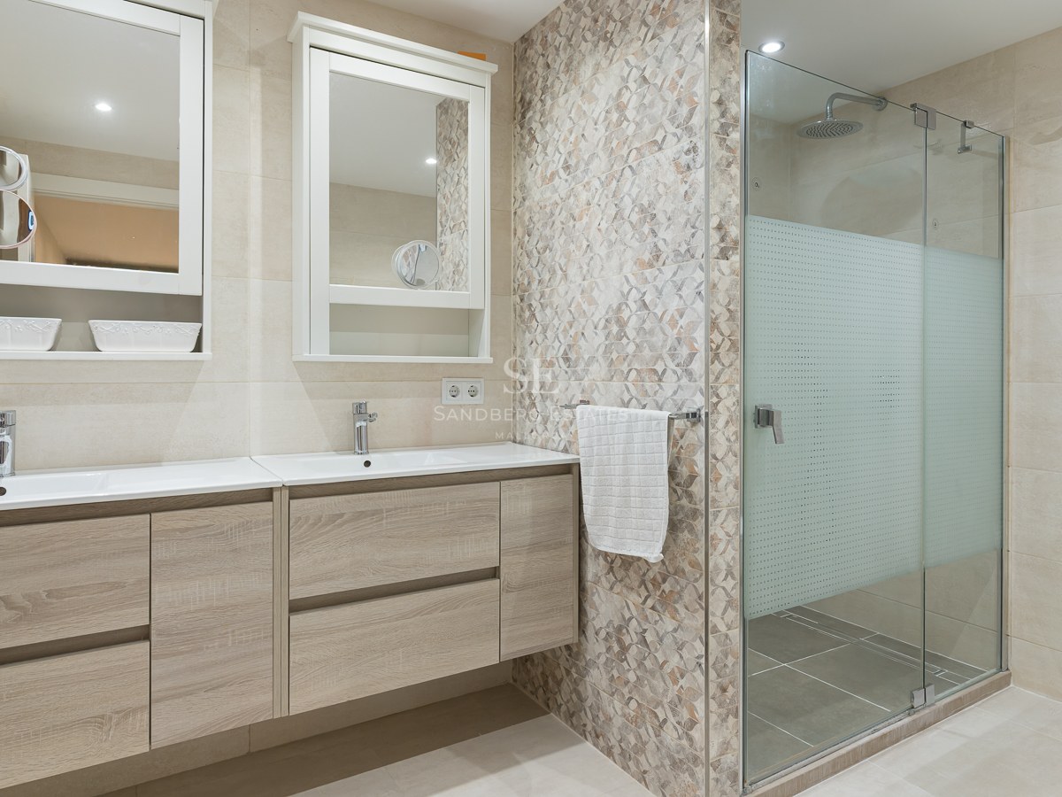 Bright master bathroom featuring a light wood double vanity, two mirrors, and a glass-enclosed walk-in shower.