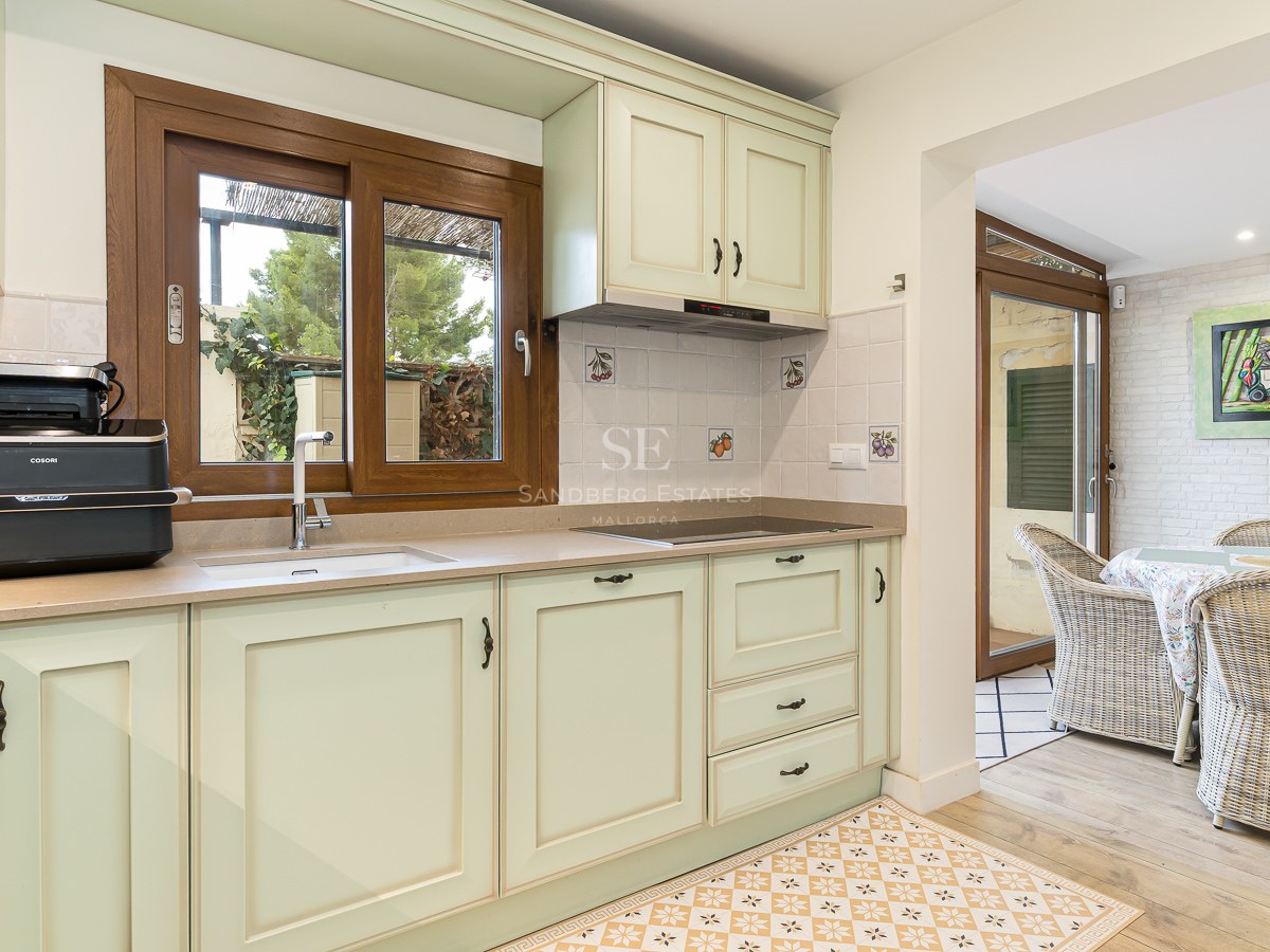 Bright kitchen with mint green cabinets, wooden window, and patterned floor leading to a dining area with wicker chairs.