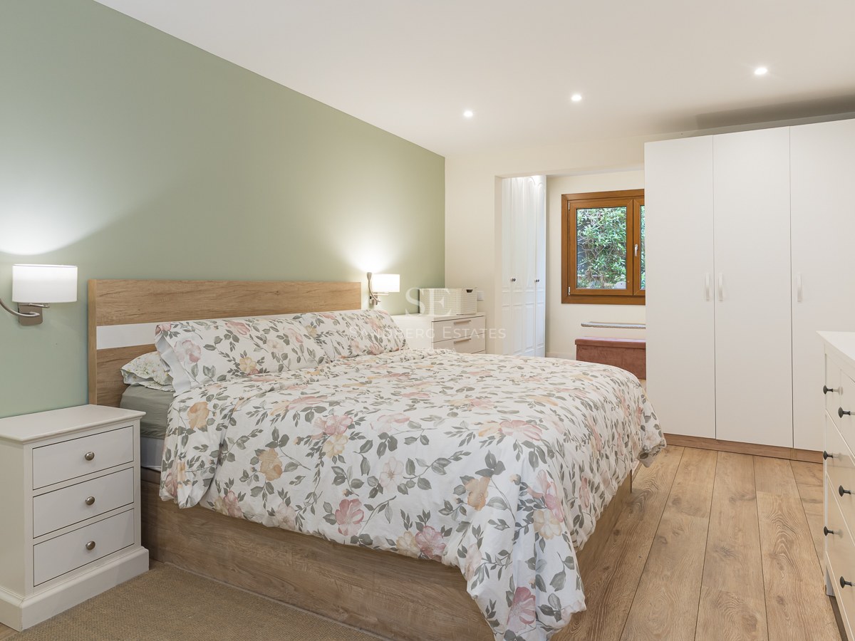 Modern bedroom featuring a floral bed, sage green wall, white furniture, and light wood flooring.