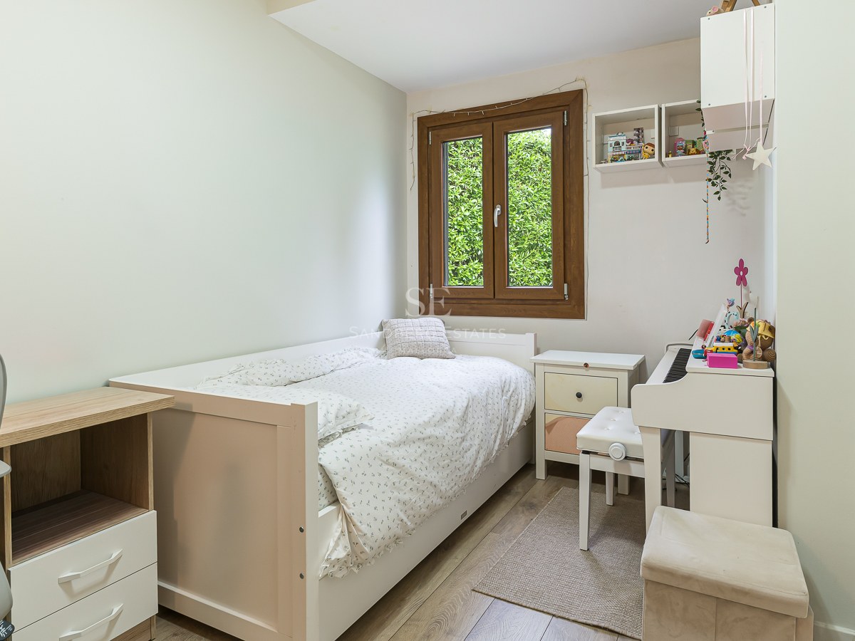 Bright bedroom with a single white bed, a desk, a white digital piano, and a window showing green foliage.