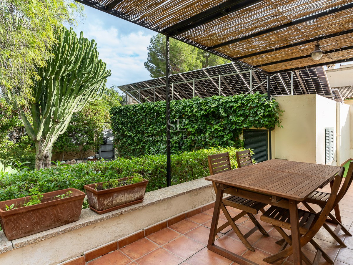 Wooden dining table under a bamboo pergola on a terracotta terrace surrounded by lush greenery and solar panels.