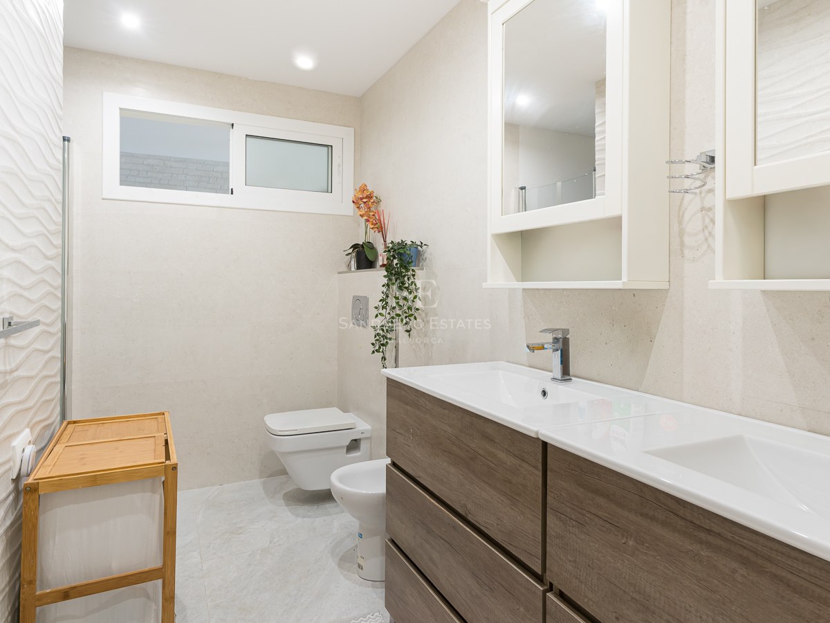 Modern bathroom with wood-finish double vanity, textured wall tiles, wall-hung toilet, and bidet.