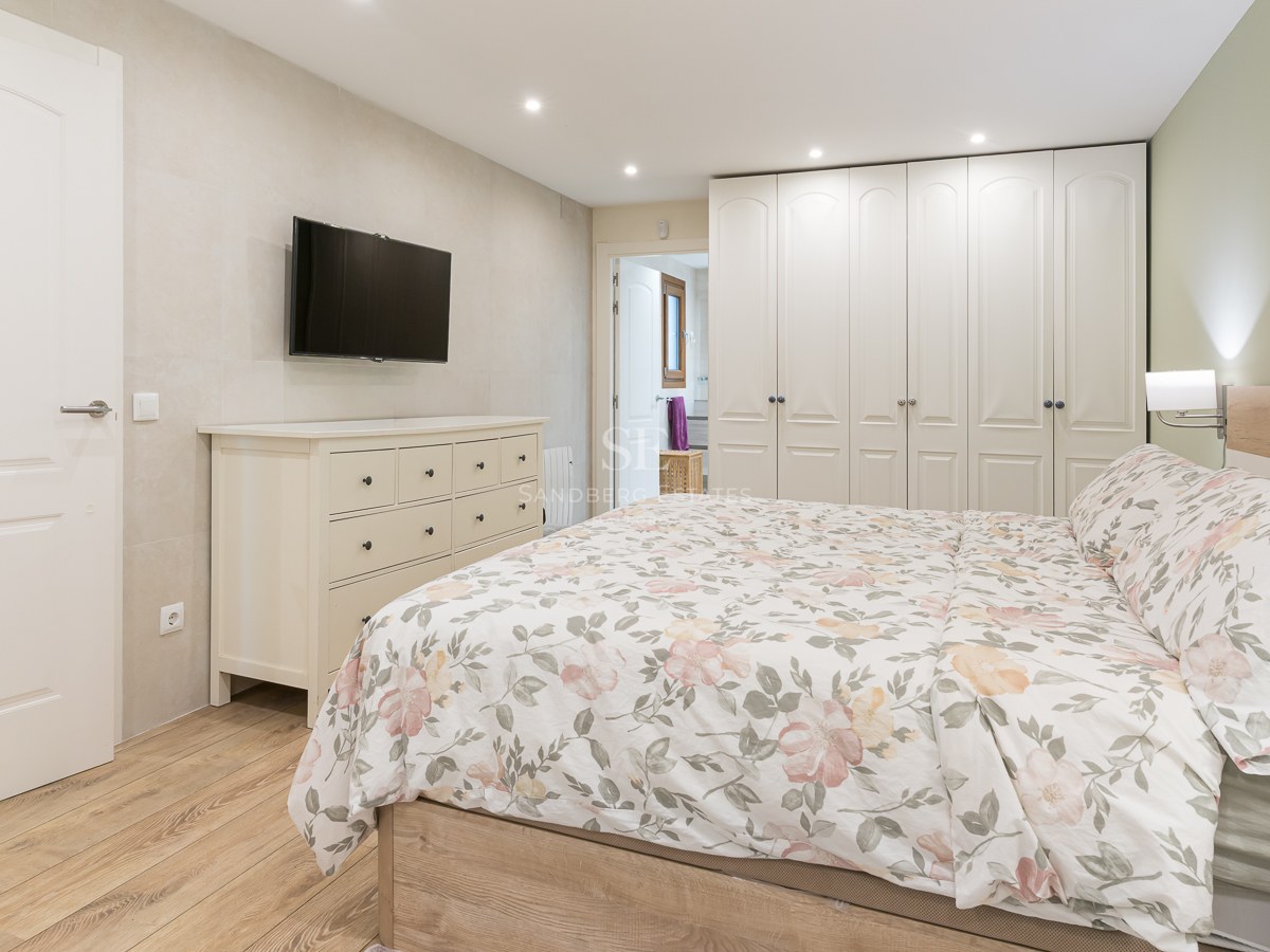 Contemporary bedroom with floral bedding, white dresser, wall-mounted TV, and large floor-to-ceiling wardrobes.