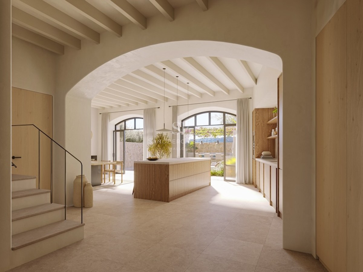 Minimalist kitchen with wooden island, beamed ceiling, and large arched doors opening to a terrace.