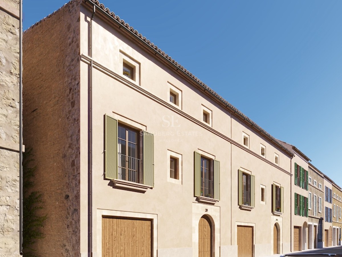 Facade of a beige Mediterranean building with green shutters, wooden doors, and a classic car on the street.
