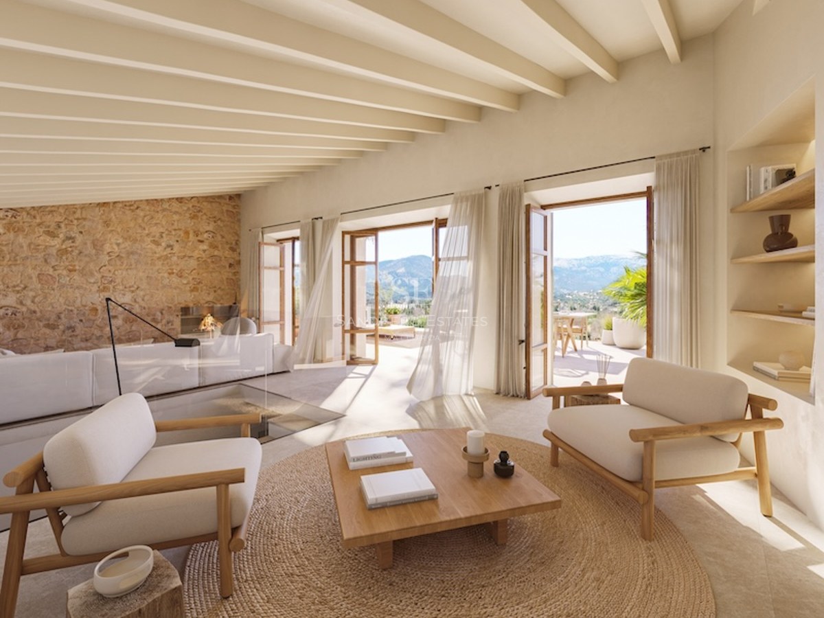 Spacious living room with wood beams, stone wall, and mountain views through open French doors.