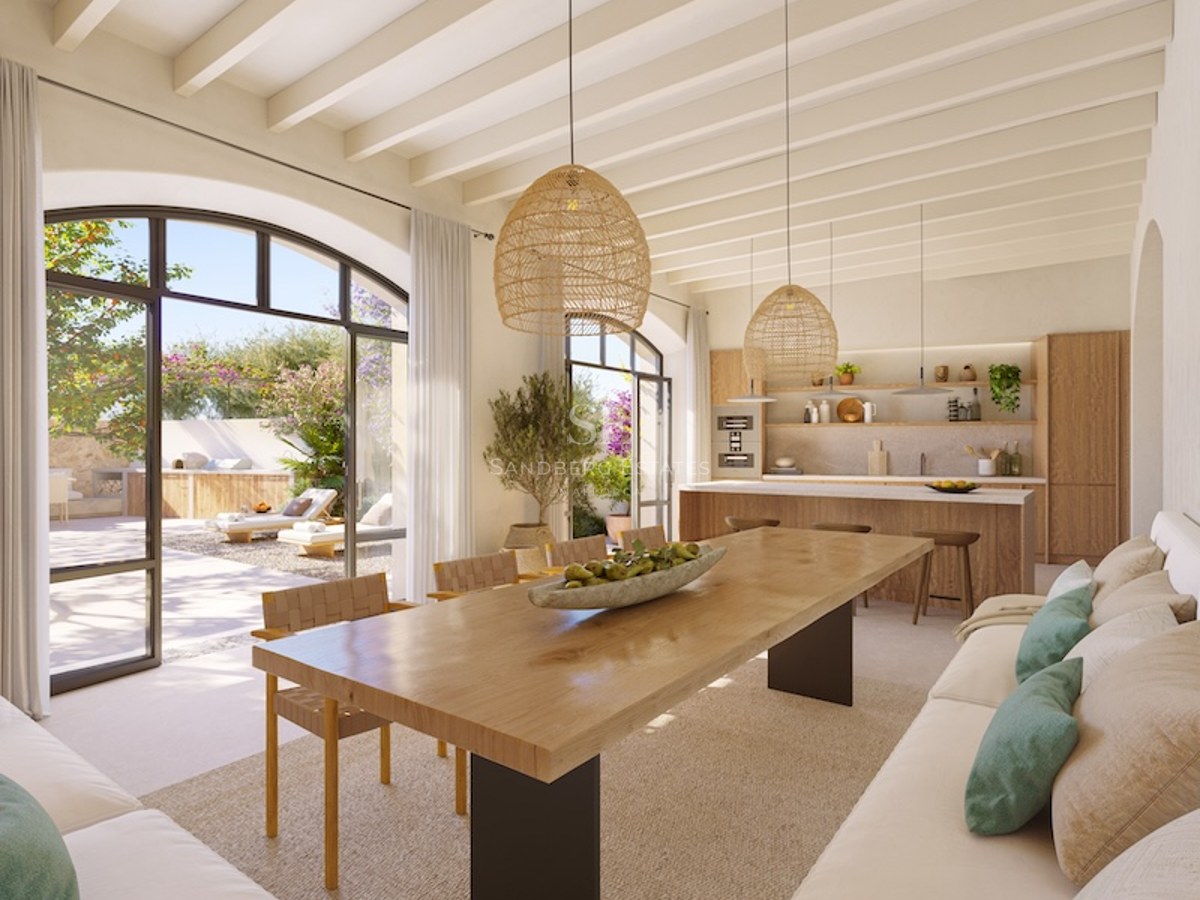 Open-concept living space with wood table, white sofas, and large arched windows facing a sunny garden.
